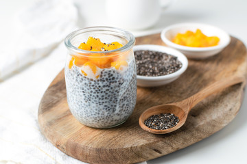 Chia pudding in glass jar with almond milk and mango on white background