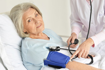 Obraz premium Portrait of senior woman in hospital with caring doctor measuring pressure