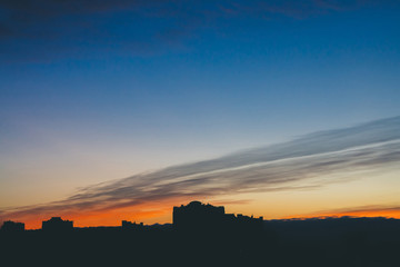 Cityscape with wonderful varicolored vivid dawn. Amazing dramatic blue cloud sky above dark...