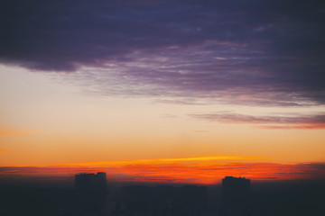 Cityscape with wonderful varicolored fiery dawn. Amazing dramatic multicolored cloudy sky. Dark silhouettes of city building roofs. Atmospheric background of sunrise in overcast weather. Copy space.