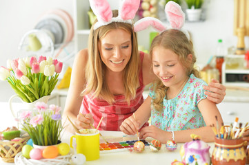 Mother with daughter wearing rabbit ears decorating Easter eggs
