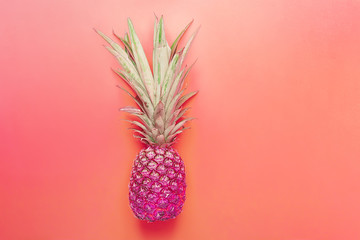 Bright purple neon color pineapple on gradient pink coral background. Long bushy green leaves....