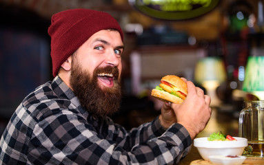 Hipster hungry man eat burger. Man with beard eat burger menu. Brutal hipster bearded man sit at...