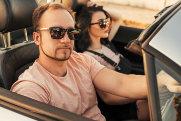 Gorgeous sexy copule of man and woman on a vacation car trip in summer day. Luxury grey sport car....