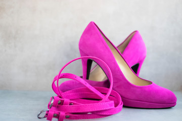 Obraz na płótnie Canvas Bright pink high-heeled shoes and a pink belt on gray background.