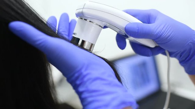 doctor dermatologist diagnoses the structure of the hair of a young pretty girl with a special tool - a trichoscope. Trichology, trichogram