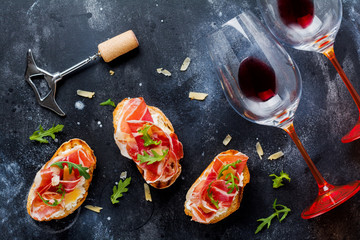 Open ham sandwiches, arugula and hard cheese, served on  wooden stand with aglass of red wine on...