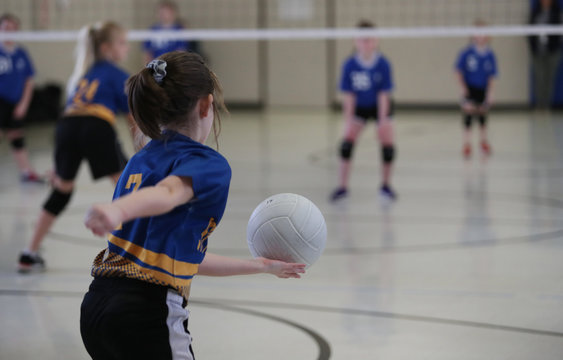 young girls serves a volleyball