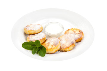 cheese pancakes sprinkled with powdered sugaron on a white plate with sour cream, decorated with mint leaves on a white background