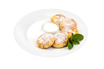 cheese pancakes sprinkled with powdered sugaron on a white plate with sour cream, decorated with mint leaves on a white background