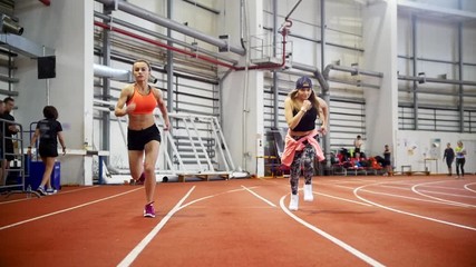 Two young athletic women prepares to run on a running track and synchronously start running