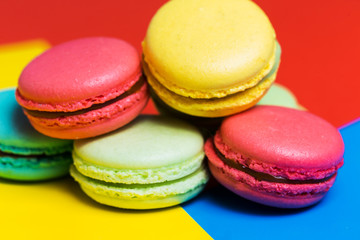 Obraz na płótnie Canvas Colorful macarons cakes on a blue background, closeup pink, yellow green French dessert