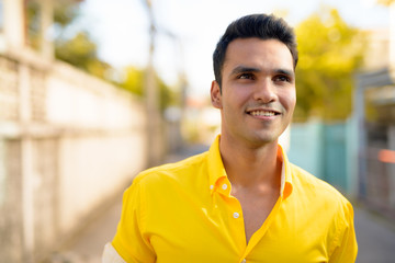 Face of young happy Indian man thinking in the streets outdoors