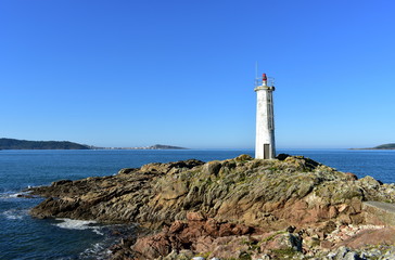 Bay with white lighthouse on the rocks. Blue sea, sunny day. Galicia, Spain.