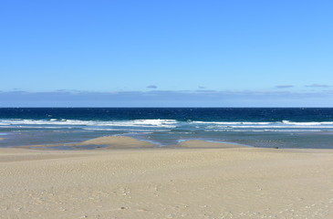 Beach with golden sand and blue sea with waves and foam. Clear sky, sunny day. Galicia, Spain.