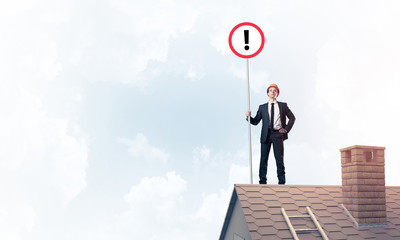 Businessman on house top showing sign with exclamation mark. Mix