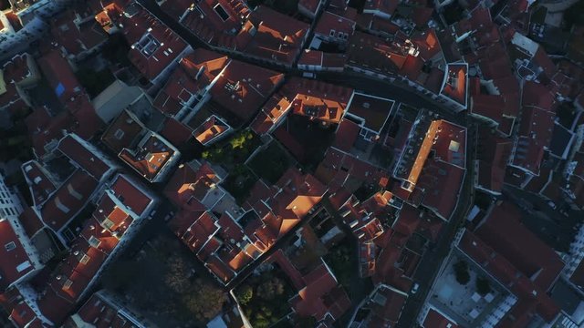Aerial top down view; Lisbon landmark with tiny houses, moorish architectural elements; drone flight over picturesque labyrinth of narrow streets small square, evening time Portugal, camera moves away