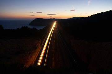 Landscape at dusk next to the Mediterranean coast with train light moving between two tunnels