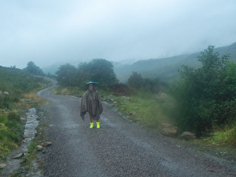 girl with umbrella hat standing in the rain in the middle of a hiking path