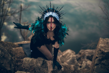 A woman in the image of a fairy and a sorceress standing over a lake in a black dress and a crown.