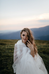 Fototapeta na wymiar Stylish bride standing on beautiful landscape of mountains on sunset