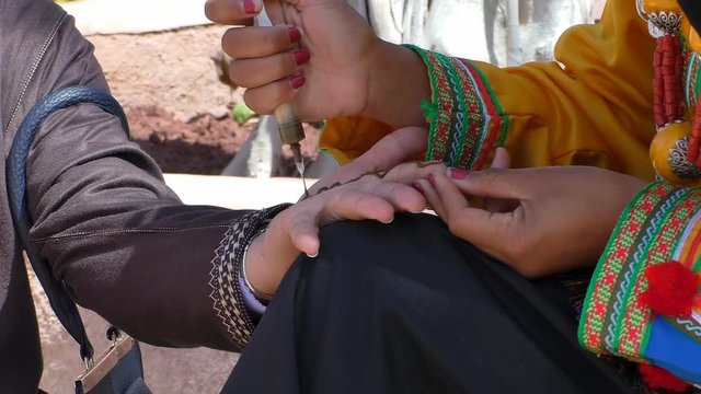 Woman in traditional Berber clothing is decorating hand with henna outdoors in Morocco