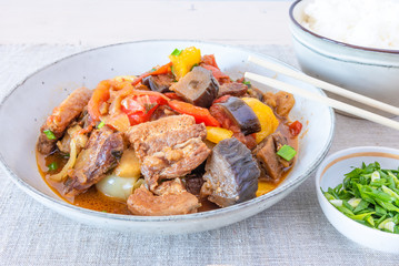 Fried pork with eggplants and sweet peppers in a large bowl and a cup of rice - a traditional Asian dish