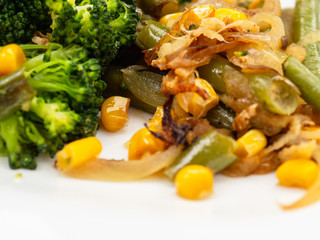 cooked vegetables broccoli, carrots, green beans, corn on a white plate. macro