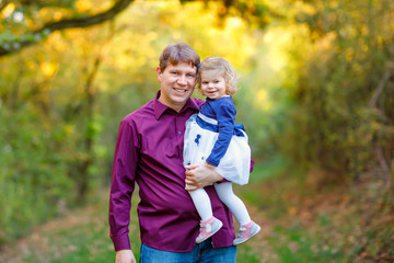 Naklejka na ściany i meble Happy young father having fun cute toddler daughter, family portrait together. man with beautiful baby girl in nature and forest. Dad with little child outdoors, hugging. Love, bonding.