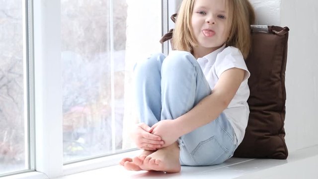 The little girl is sitting on the windowsill with different emotions of the face.