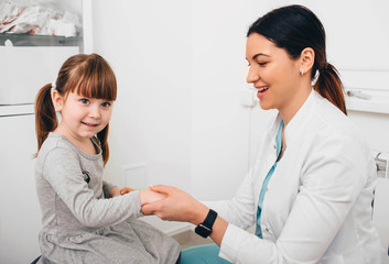 Cheerful pediatrician greets a little patient's. Doctor holding child's hand in comfort