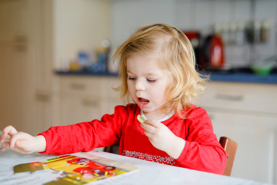 Adorable little toddler girl blonde child, playing with puzzles at home or kindergarten. Cute happy healthy child puzzling and making picture. Development and education step for baby