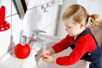 Cute little toddler girl washing hands with soap and water in bathroom. Adorable child learning...