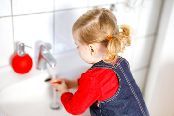 Cute little toddler girl washing hands with soap and water in bathroom. Adorable child learning cleaning body parts. Morning hygiene routine. Happy healthy kid at home or nursery.