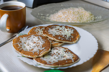Fresh fried pancakes lie on a plate and sprinkled with grated cheese.
