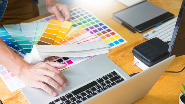 graphic designer team working on web design using color swatches editing artwork using tablet and a stylus At Desks In Busy Creative Office.