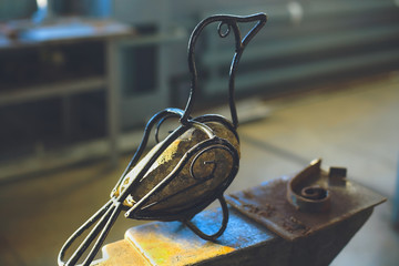 Homemade artificial bird of wire and stone body sitting on an anvil.