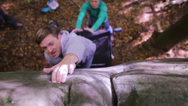 boulder climbing in the woods. climber trying to climb on a boulder and friends insure the bottom. unsuccessful attempt.