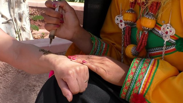 Close up shot of woman wearing traditional Moroccan Berber clothes decorating tattooing hand with henna outdoors