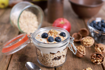 light healthy breakfast  with yogurt on oatmeal muesli , blueberries and walnuts in a glas on a rustic wooden table. close up