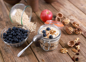 light healthy breakfast  with yogurt on oatmeal muesli , blueberries and walnuts in a glas on a rustic wooden table