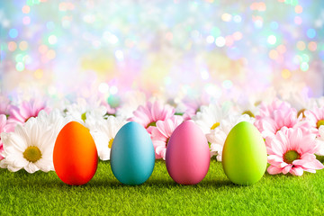 Pink and white flowers and Easter eggs on the grass and colorful abstract background