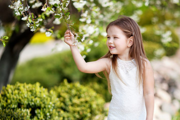 Prettyl smiling little girl in cream dressin the blossom garden