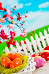 Colorful Easter eggs, nest and fence on wooden table and nature background