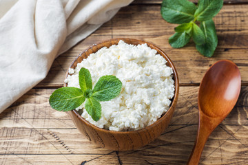 Homemade cottage cheese with mint in a bowl on old wooden table.