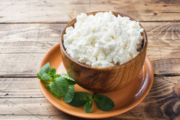 Homemade cottage cheese with mint in a bowl on old wooden table. Copy space