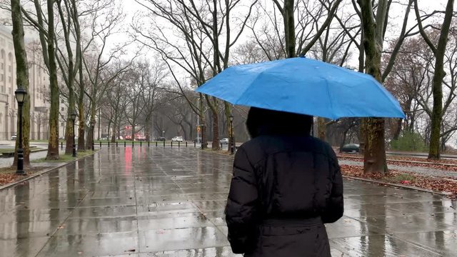 Back view of a woman walking in a city park while raining. Loneliness and isolation concept