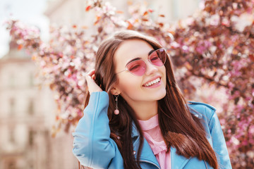 Young happy smiling, laughing lady wearing stylish pink cat eye sunglasses, earrings, blue jacket,...