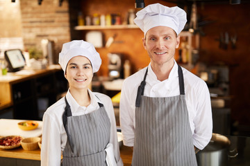 Waist up portrait of two professional cooks posing in restaurant kitchen smiling at camera, copy...
