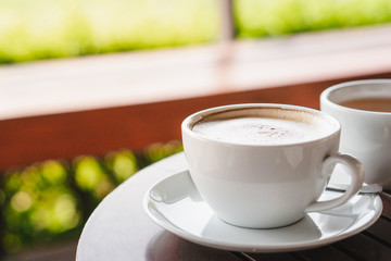 Hot coffee, white cups, plate, spoon and tissue all on the wooden table.